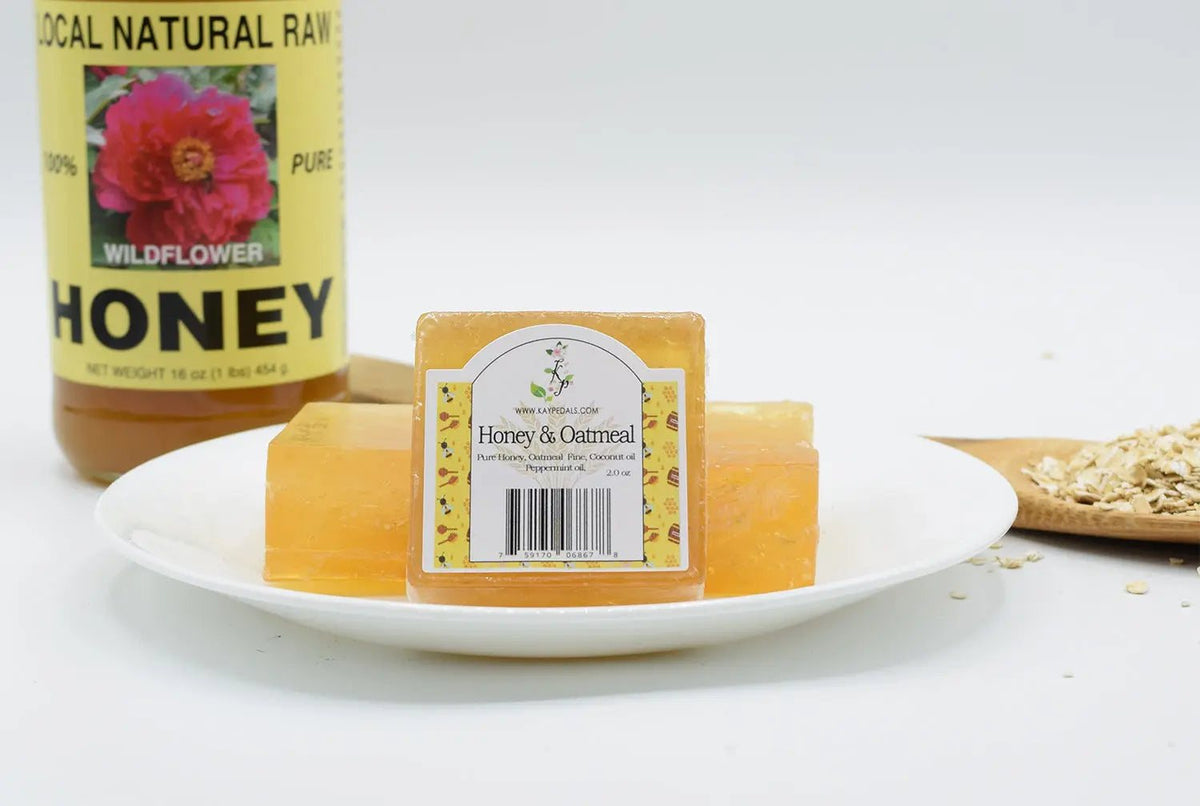 Honey and Oatmeal Soap bars in translucent amber color with a white label, displayed with a honey jar and oats on a plate.