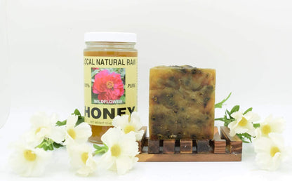 Chamomile Natural Handcrafted soap bar in a brownish color with embedded flower buds on a wooden soap dish beside a jar of local raw honey and white flowers.