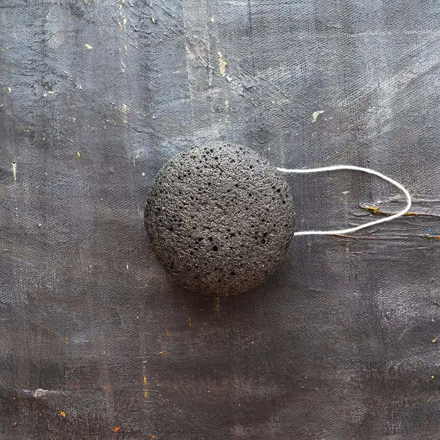Konjac Facial Sponge in charcoal color, round porous texture with a white hanging string attached.