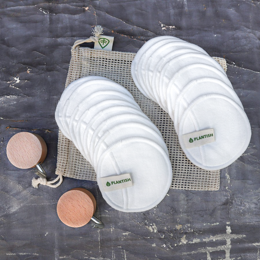 100% Cotton Facial Rounds set with white, reusable cotton pads, organic mesh bag, and wooden wall hooks for drying and storage.