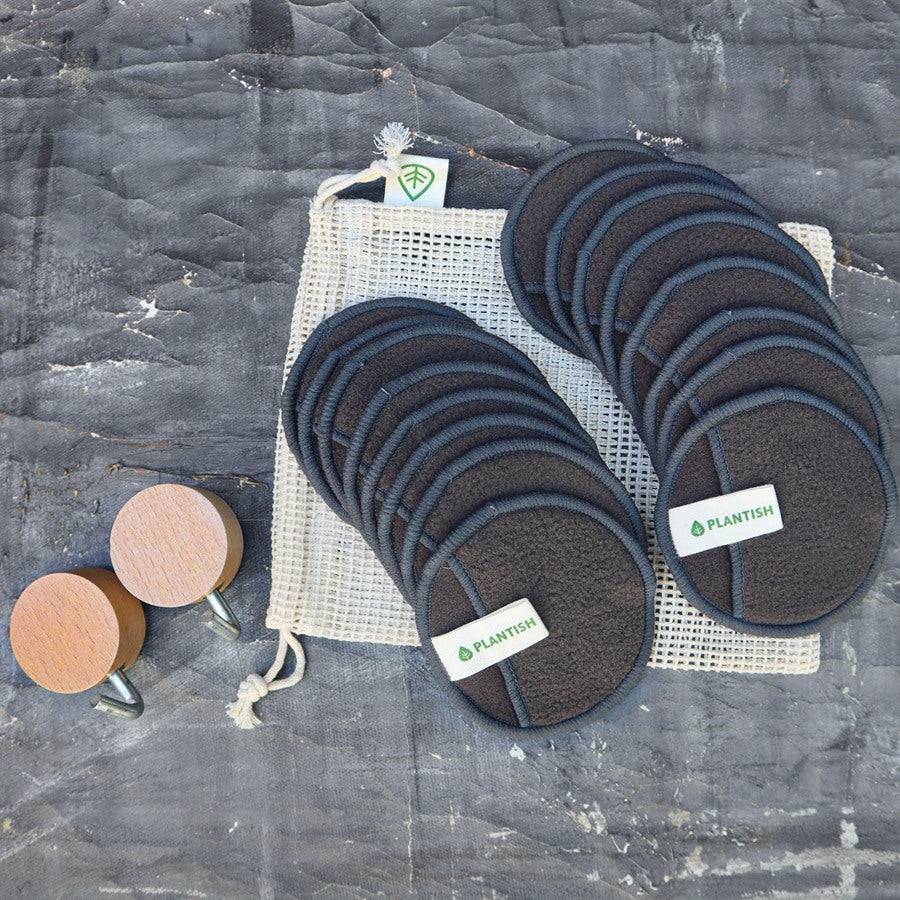 Bamboo Charcoal Facial Rounds Set featuring dark gray reusable cotton pads with fabric labels, an organic mesh bag, and wooden wall hooks for drying.