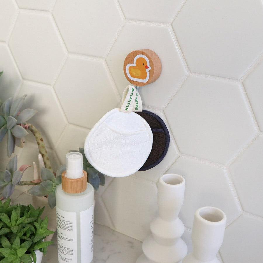 Bamboo Charcoal Facial Rounds Set with white and black reusable cotton pads hanging on a wooden wall hook with a duck design.